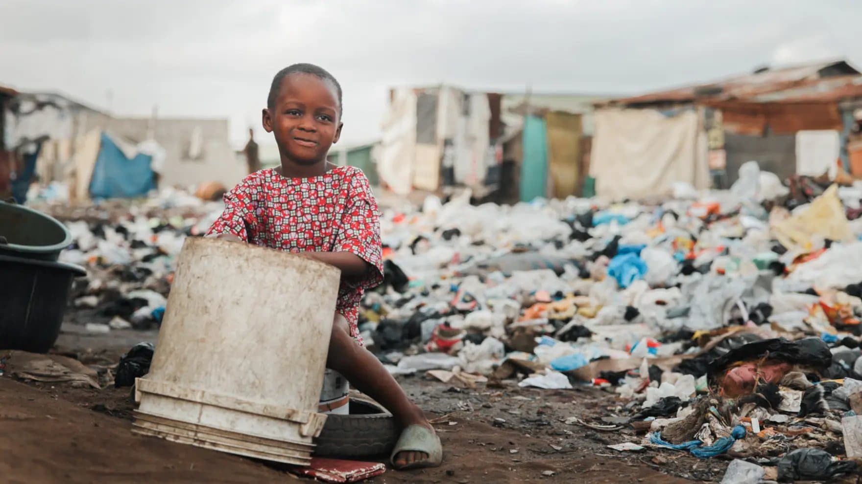 A child playing with plastic drum in garbage landfill