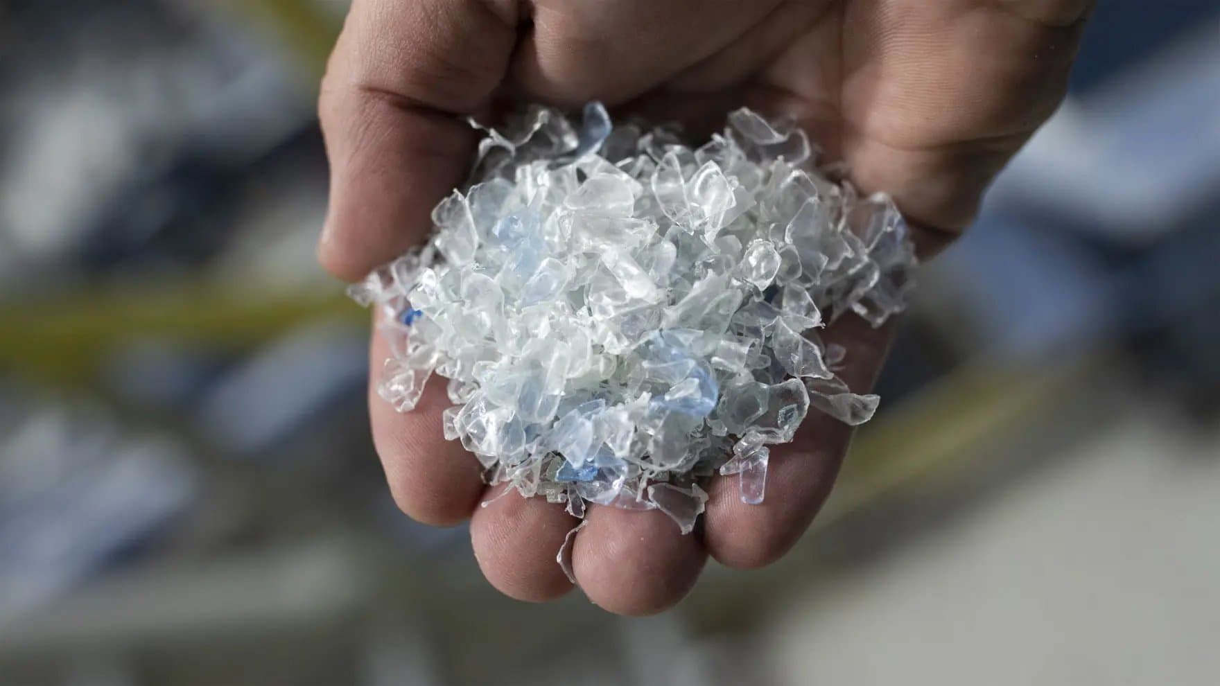 A hand holds a pile of translucent, shredded plastic pieces, with a blurred background.
