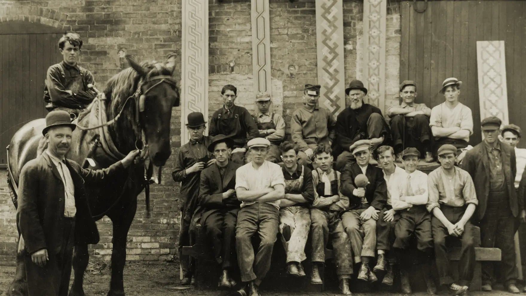 A group of men pose outdoors, including one man holding a horse's reins while another sits on it. They stand against a brick wall with decorative patterns.