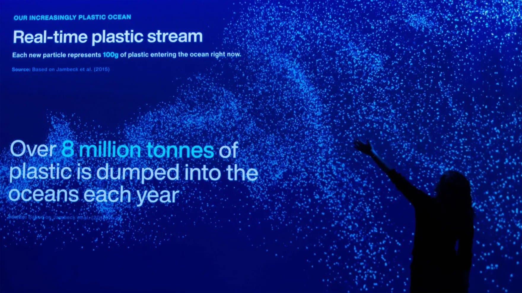 Silhouette of a person reaches toward a screen displaying blue particles, representing plastic in the ocean. Text reads: "Real-time plastic stream: Over 8 million tonnes of plastic is dumped into the oceans each year."