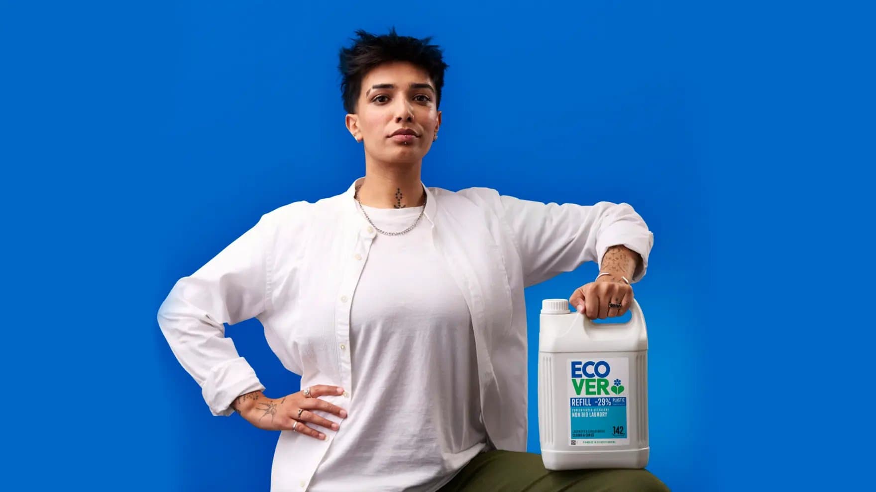 A person holds a large white container labeled "ECOVER" against a bright blue background. The text reads, "REFILL -29% PLASTIC, CONCENTRATED FORMULA, NON-BIO LAUNDRY, 142 WASHES."