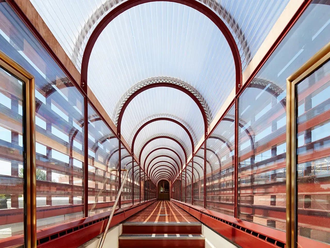 A covered walkway extends forward, featuring red metal arches and transparent walls. The path leads into the distance, surrounded by a reflective environment creating a tunnel-like effect.