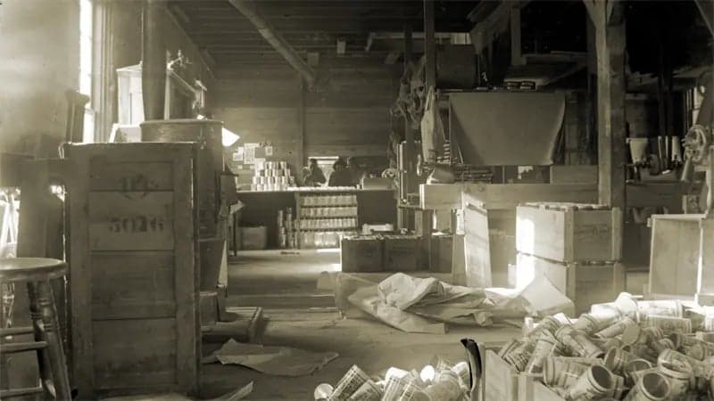 Vintage sepia-toned photo of factory with boxes, crates, and drop cloths