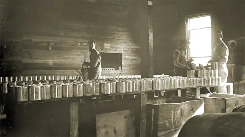 Vintage sepia-toned photo of factory tables lined with metal tins